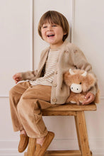 
                        
                          Load image into Gallery viewer, Child sitting on a wooden stool holding a fluffy toy, wearing a beige cardigan and brown pants.
                        
                      