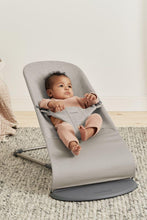 
                        
                          Load image into Gallery viewer, Baby in a gray baby bouncer on a carpeted floor with a neutral background
                        
                      