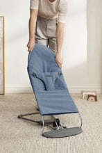 
                        
                          Load image into Gallery viewer, mum folding a blue and gray bouncer on a carpeted floor.
                        
                      