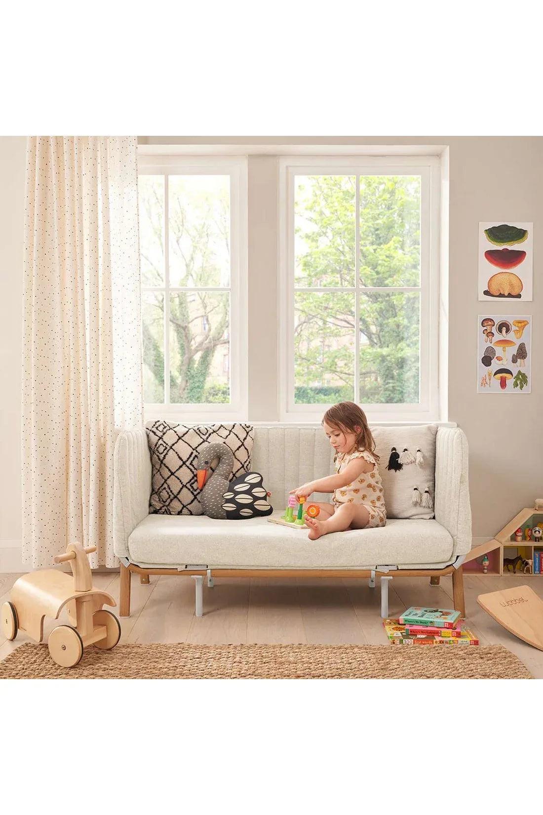 Tutti bambini Cozee XL bedside Cot Color in walnut and Ecru white Crib & Cot toddler sitting on the sofa